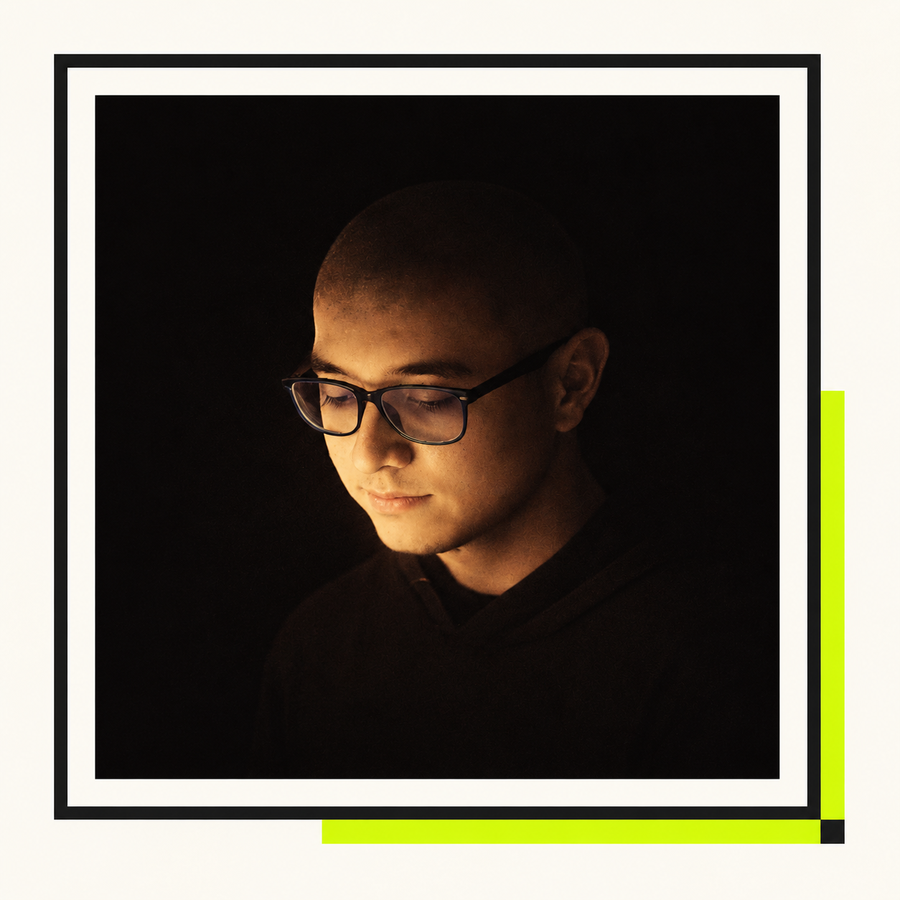 Retrato de Miguel Bracamontes usando gafas, con iluminación tenue sobre fondo oscuro.